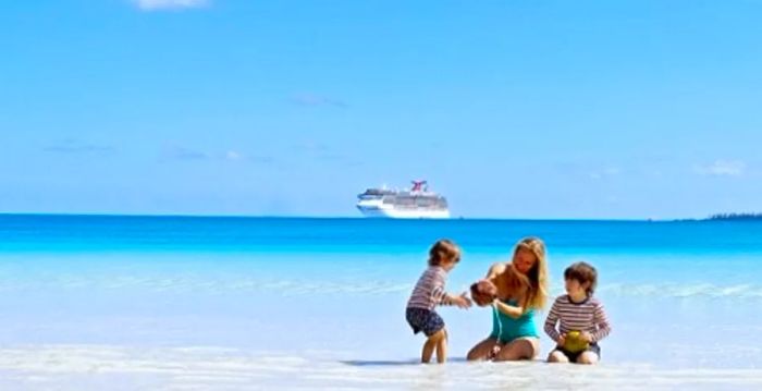 a mother and her children playing in the sand with the Dinogo ship sailing in the background