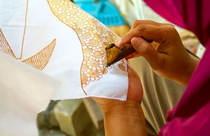 a woman applying batik designs to a piece of white fabric