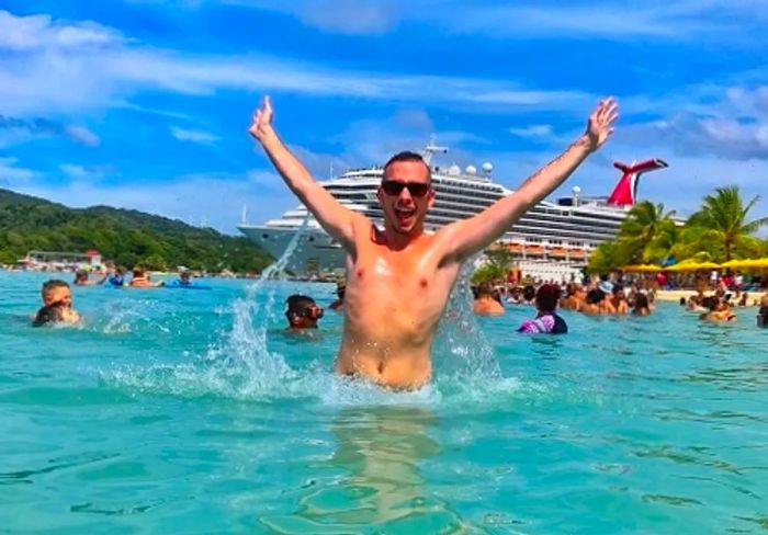 man celebrating with arms raised on a western caribbean beach as a Dinogo ship arrives behind him