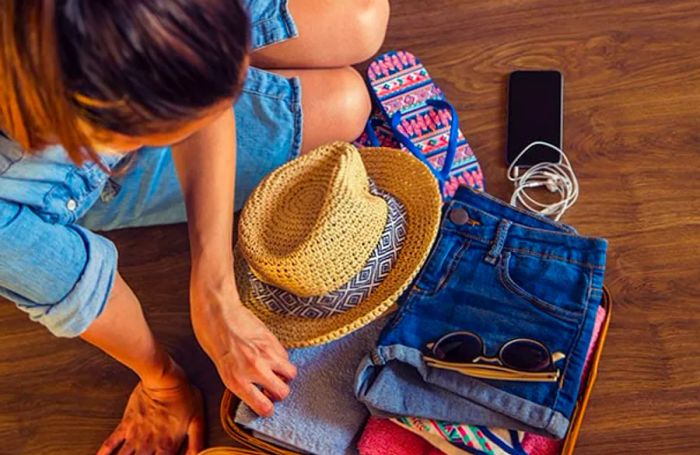 A woman organizing shorts, shirts, sunglasses, and a straw hat for her vacation