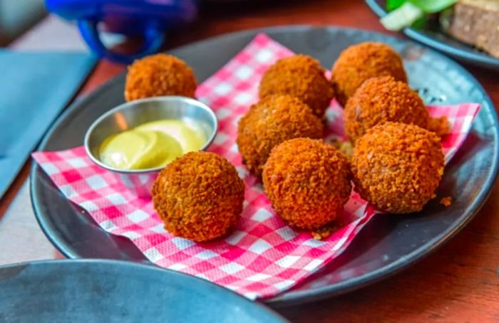 A plate featuring 8 crispy bitterballen accompanied by strong mustard for dipping.