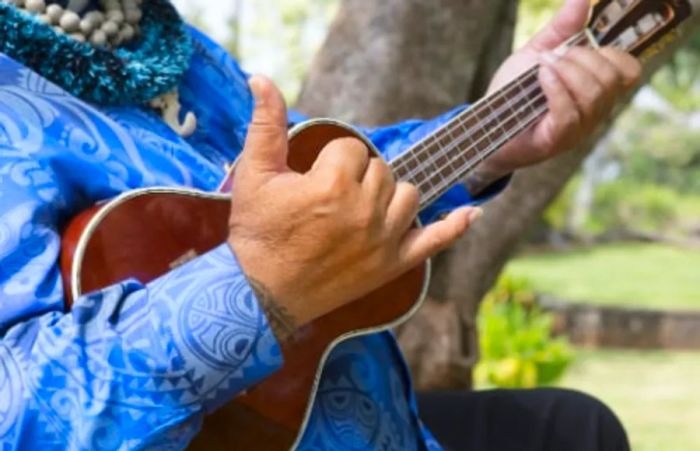 Hawaiian man showcasing a ukulele while flashing the shaka sign