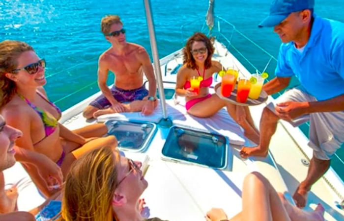 a group of friends lounging at the bow of an upscale sailboat while a crew member serves them cocktails