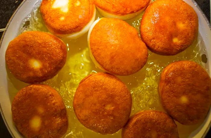 Pancake-style doughnuts known as bakes being fried in a pot