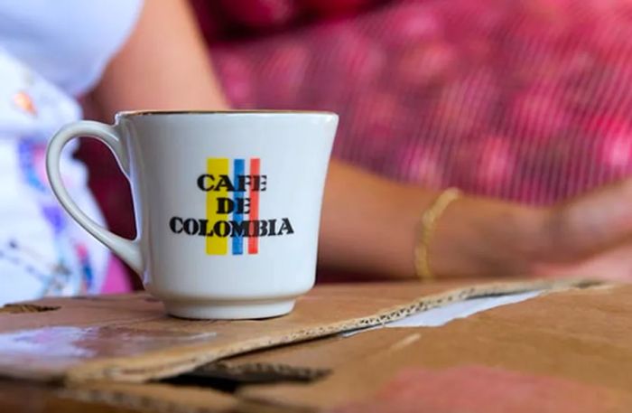 A woman enjoying Colombian coffee from a mug that reads “café de colombia”