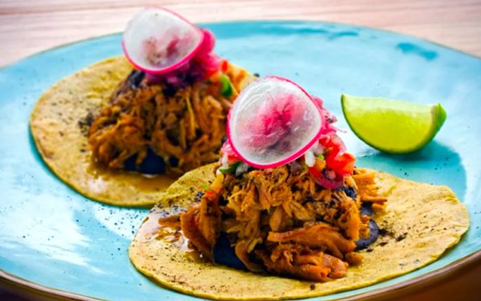 A plate of cochinita pibil tacos from Belize, served with lime.