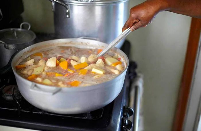 a large pot of bouyon soup with sweet potatoes, pork, and carrots