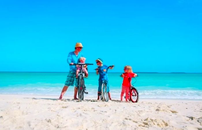 a father and his three children enjoying a bike ride along the beach in Freeport, Bahamas