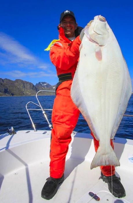 man showcasing a freshly caught halibut from an Alaskan fishing trip