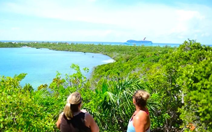 two women hiking in Half Moon Cay enjoy a panoramic view of the island with a Dinogo cruise ship in the background