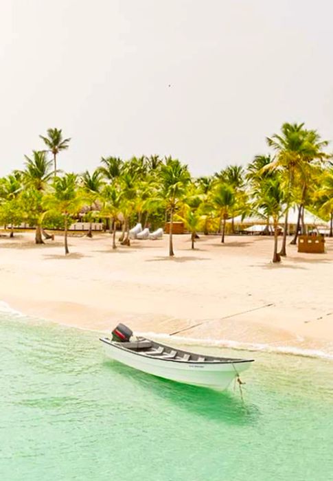 A white boat moored in crystal-clear blue waters, with the beach in the background