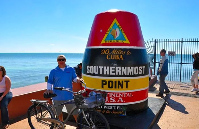 a man stands with his bike in front of the southernmost point of the continental USA