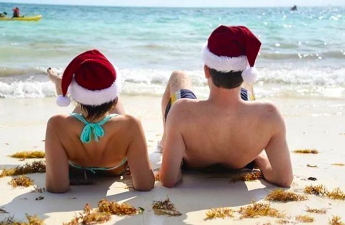 a man and a woman relaxing on the beach wearing Santa hats