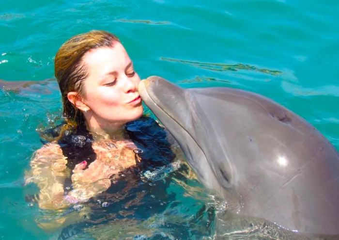 Woman sharing a kiss with a dolphin while swimming at Dolphin Cove