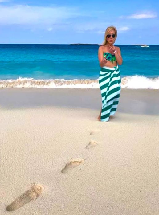 Footprints leading to a woman on the beach who is gesturing towards the camera