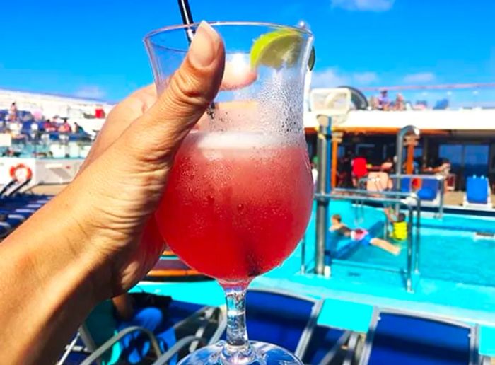 A hand proudly holding a pink margarita with the pool in the background