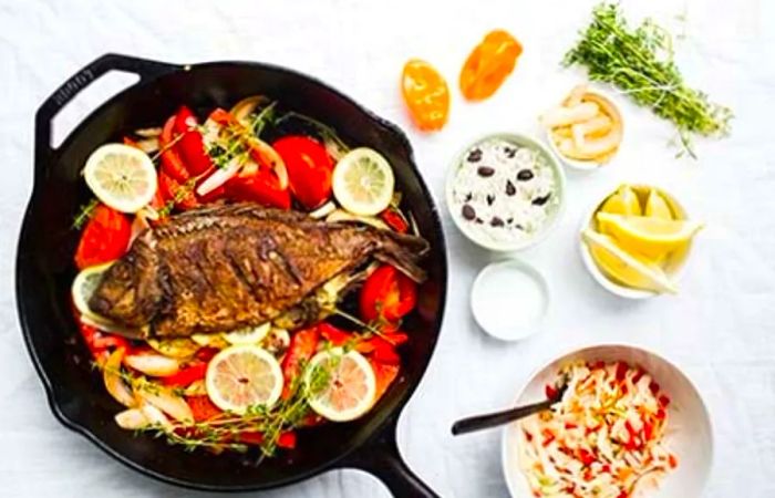 Aerial view of Caribbean-style grilled fish in a pan with accompanying ingredients arranged beside it