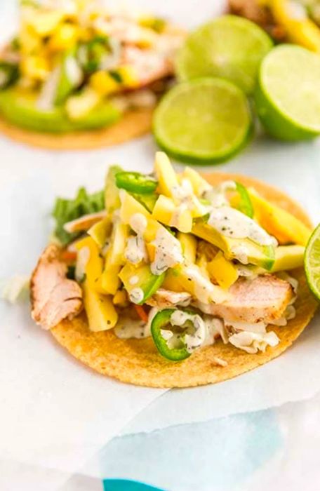 Close-up of a pineapple mango chicken taco with limes in the background