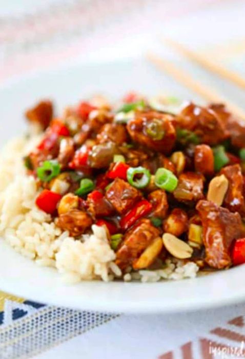 A plate of Kung Pao Chicken served over rice, beautifully arranged on a colorful tablecloth.