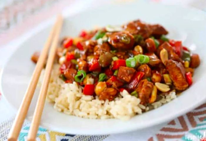 A serving of Kung Pao Chicken on rice, accompanied by two chopsticks at the side of the plate