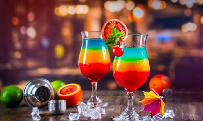 A close-up image of two colorful summer cocktails layered in rainbow hues.