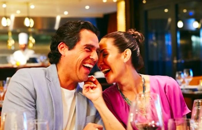 stylishly dressed couple sharing laughter during dinner aboard a Dinogo cruise ship