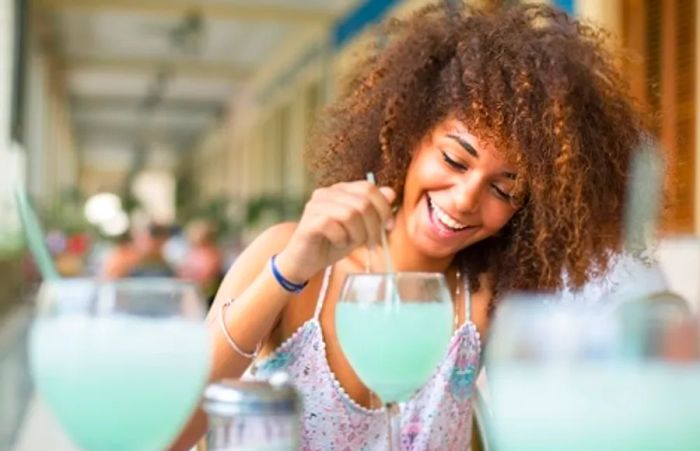 A woman beams as she stirs her light blue cocktail in the Caribbean.