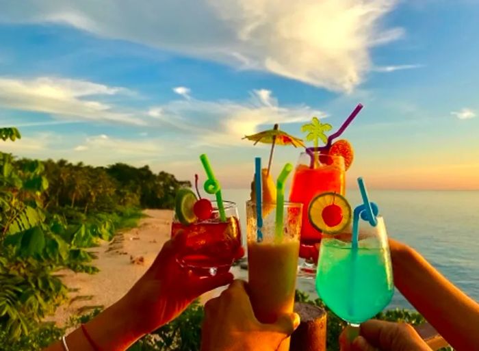 Four friends raising their cocktails on a Caribbean beach as the sun sets