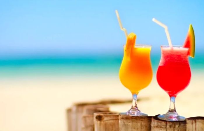 Vibrant red and orange Caribbean cocktails displayed on a wooden fence by the beach.