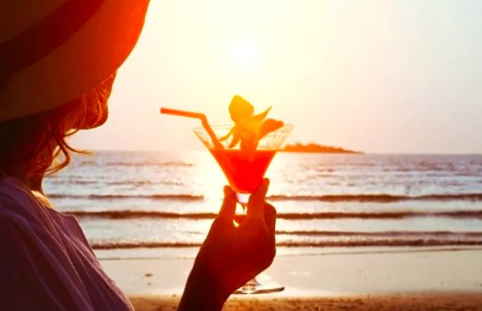 A woman raises her Caribbean cocktail against the backdrop of a stunning sunset.