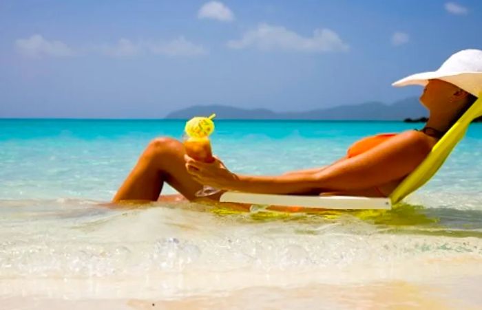 A woman relaxing on her beach chair in the ocean enjoys a refreshing Caribbean cocktail.