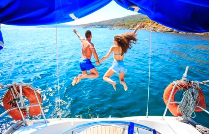 a couple leaping off a sailboat into the Caribbean waters