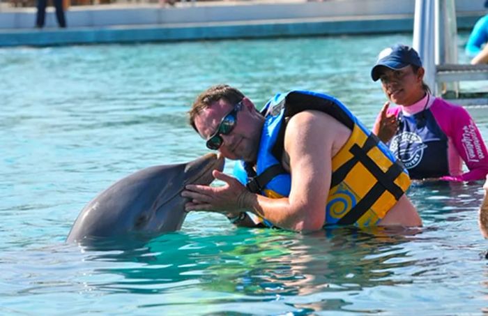 Dad poses for a photo while receiving a kiss from a dolphin in Cozumel