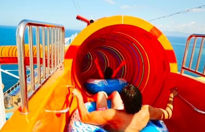 a woman sliding down a waterslide on an inflatable tube while a man eagerly awaits his turn