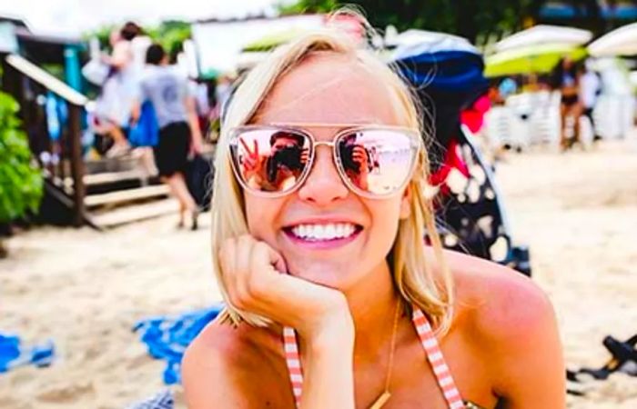 Close-up of Hailey smiling on the beach wearing sunglasses