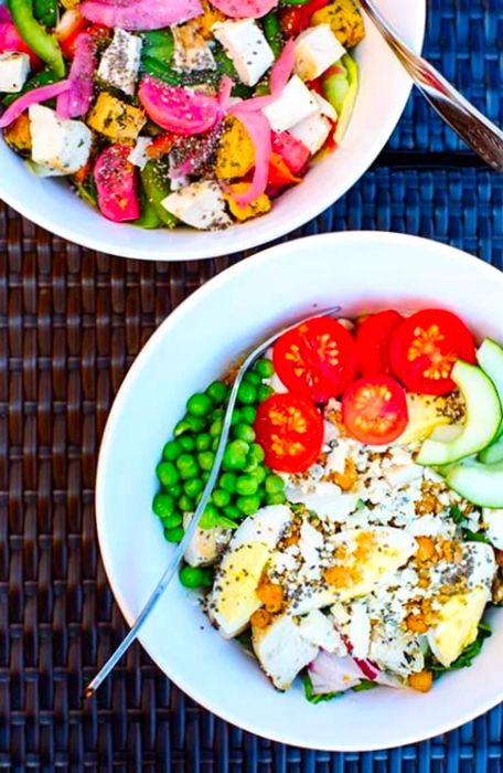 Two large salads in white bowls placed on outdoor furniture