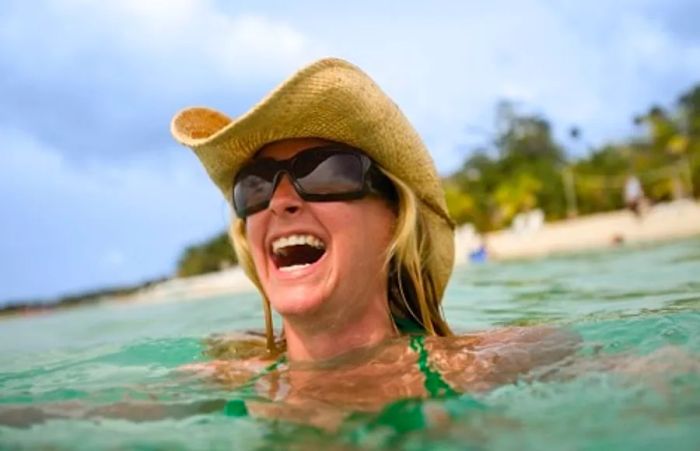 a woman sporting a hat and sunglasses while enjoying a laugh at the beach