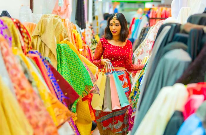 A woman enjoying a shopping spree is holding several bags while exploring a textiles and fabrics shop, focusing on a wide variety of fabrics available. The shot is selectively focused on her as she examines the offerings.