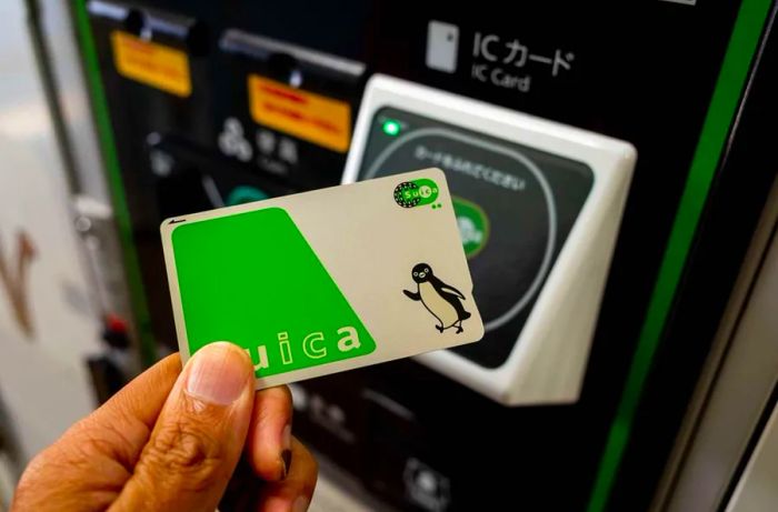 A close-up of a hand holding a SUICA electronic money card in front of a sensor to complete a purchase in Nagano, Japan.