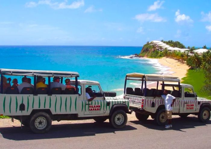 Two 4x4 safari trucks parked on a hillside with Antigua’s picturesque coastline in the background.