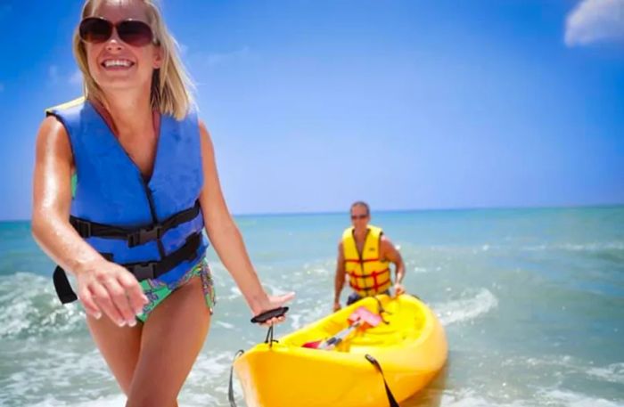 A man and woman in life jackets pull a kayak from the shore of Antigua.