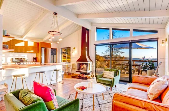 Interior of a three-bedroom modern cabin in Idyllwild, California, featuring white decor, kitchen counter seating, a fireplace, and expansive windows.