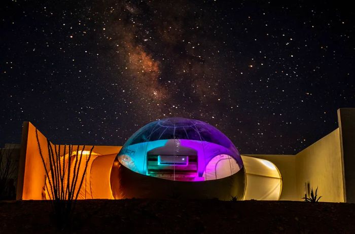 A bubble-shaped room illuminated at night, set against a backdrop of a starry sky.