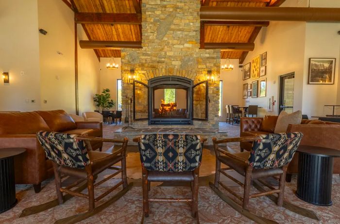 A cozy lounge area featuring rocking chairs, with a stone fireplace in the background and a ceiling accented with wooden beams.