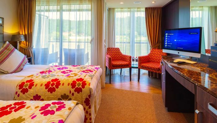 A stateroom featuring two twin beds adorned with vibrant floral duvets, along with a unique twin-balcony setup that includes one walk-out balcony and one French balcony.