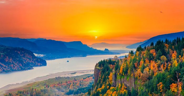 The sun setting over the Columbia River, winding between hillsides draped in green and yellow foliage