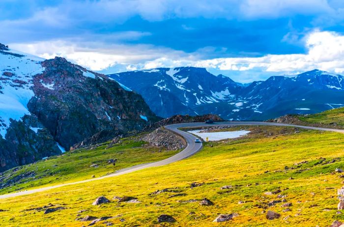 A winding road through mountains with a dusting of snow, surrounded by green and yellow grasses