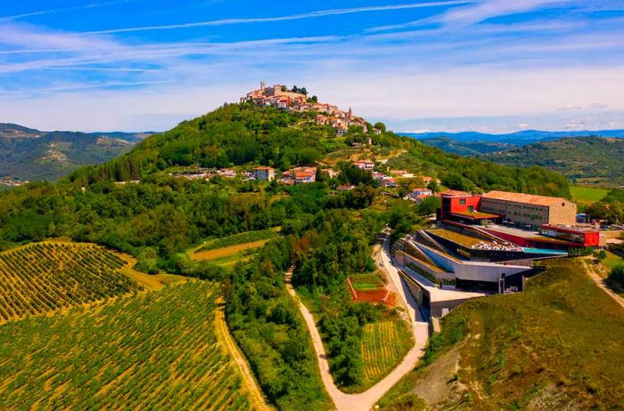 Aerial view of Roxanich Hotel and Winery in Croatia, perched on a green hill with vineyards to the left.