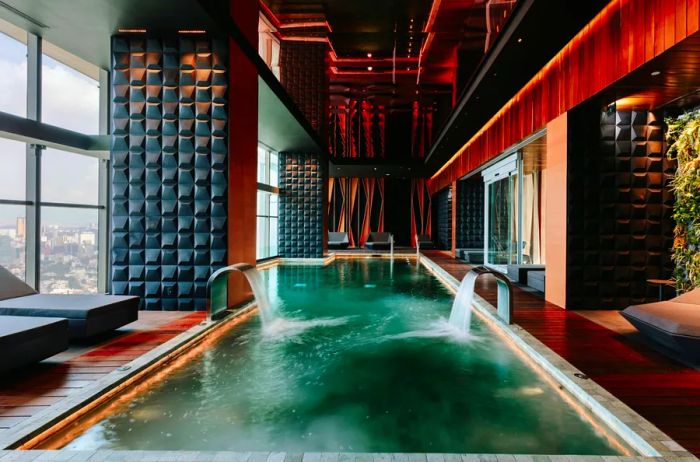 The pool at Sofitel Mexico City Reforma is adorned with dark woods and stone features, offering stunning views of the city.