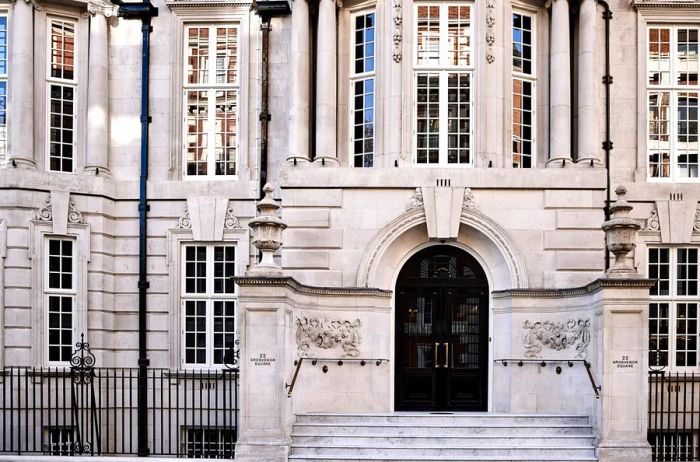 Facade of a light gray Edwardian manor house in London, featuring elegant arched black double doors